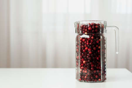 Cranberry. Small forest red berry. Cranberries in a jug and in a glass on the table. A glass of cranberries. Vitamins from nature. Selective focus.の写真素材