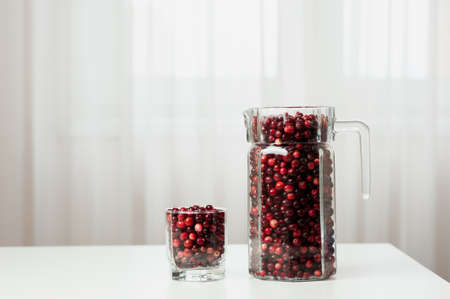 Cranberry. Small forest red berry. Cranberries in a jug and in a glass on the table. A glass of cranberries. Vitamins from nature. Selective focus.の写真素材
