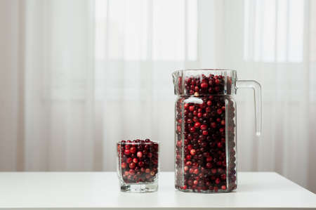 Cranberry. Small forest red berry. Cranberries in a jug and in a glass on the table. A glass of cranberries. Vitamins from nature. Selective focus.の写真素材