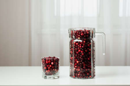 Cranberry. Small forest red berry. Cranberries in a jug and in a glass on the table. A glass of cranberries. Vitamins from nature. Selective focus.の写真素材