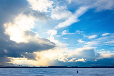 Huge yellow and white skies. tiny silhouette of a man on a frozen lake against a blue sky. a very...