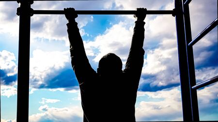 silhouette of a man on the sports ground. man pulls himself up on the horizontal bar. outdoor...
