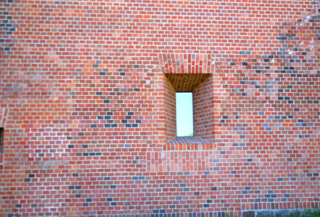 Old red brick wall with a window in the shape of a house
