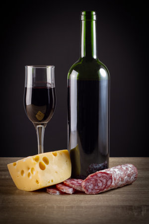 Red wine, cheese and salami on a wooden table. Black background.の写真素材