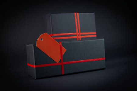 Black gift box with red ribbon on a black background. Shallow depth of field.の写真素材