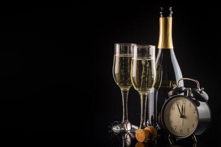 Champagne glasses and alarm clock on black background with copy space. New Year and Christmas celebration concept.の写真素材