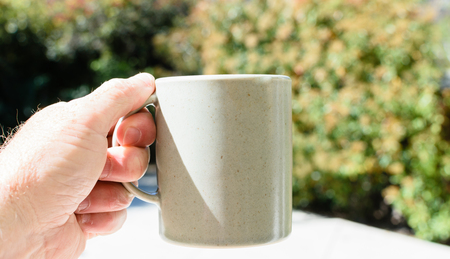 Male hand holds coffee mug outdoorsの写真素材