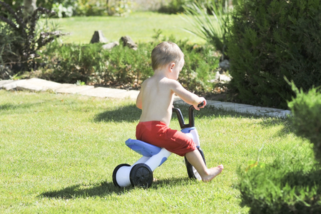 Little boy pours from a hose in the garden on a hot summer day on a green lawn, splashing waterの写真素材