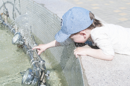 A little boy in the city plays near the fountain with waterの写真素材