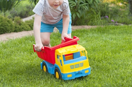 A child is playing on the grass with a big red toy carの写真素材