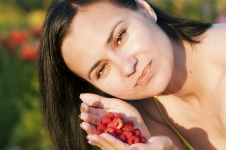 Happy beautiful girl eating raspberries, holding berries in the palm of her handの写真素材