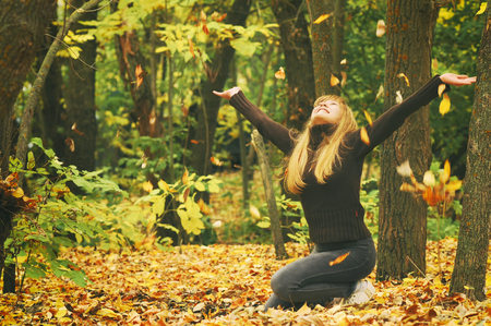 Young girl in autumn forest, throws yellow leaves, toned photoの写真素材
