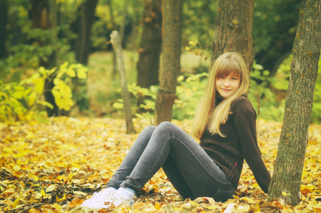 Young girl in autumn forest, throws yellow leaves, toned photoの写真素材