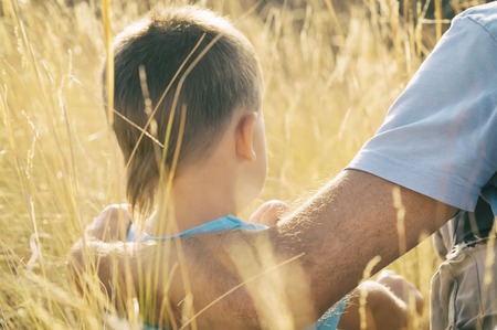 father and son are sitting in the field, father hugs his son, toned photoの写真素材