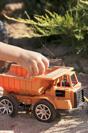 A child plays in the sand with big toy cars, an excavator, a truckの写真素材