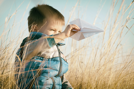 A boy is playing with a toy paper airplane against the blue sky in the fieldの写真素材