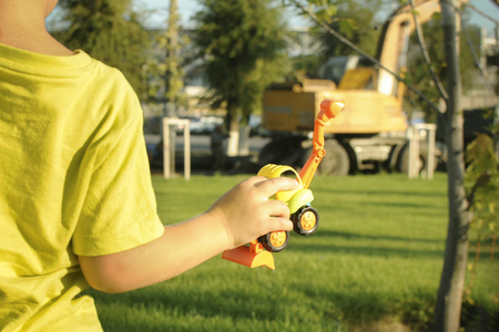 The boy observes the work of the excavator, holds a toy excavator in his handの写真素材