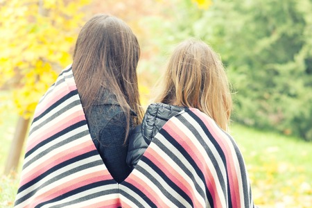 Two girls are sitting covered in a plaid in an autumn park,の写真素材