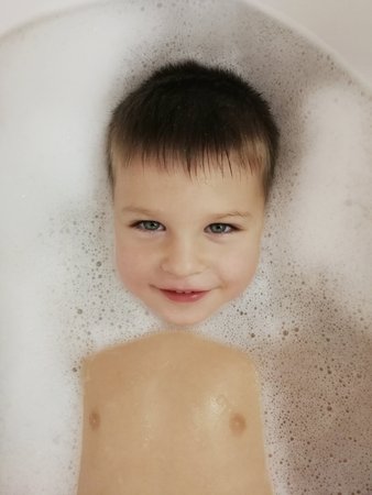 A little boy is lying in a bath with soap and water