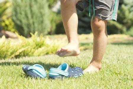 Baby legs and childrens blue slippers on the green grass in the garden, shoes for children, the concept of a healthy lifestyleの写真素材