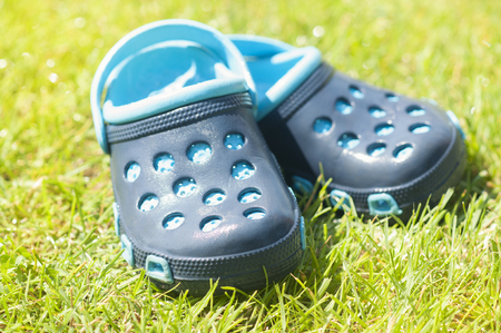 Childrens blue slippers on the green grass in the garden, shoes for children, beach fashion for kids, a concept of relaxationの写真素材