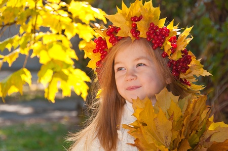Cute smiling girl in a wreath of red viburnum on the head and with a bouquet of maple leaves in the handsの写真素材