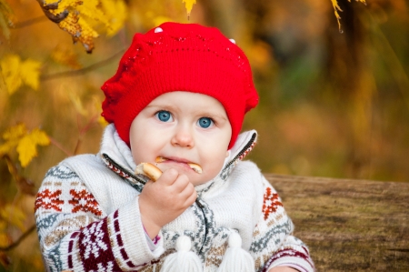 Cute little baby girl sitting in the forest and eating a bagelの写真素材
