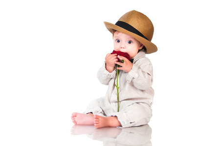 Funny baby boy in retro hat and bow tie is eating a red roseの写真素材