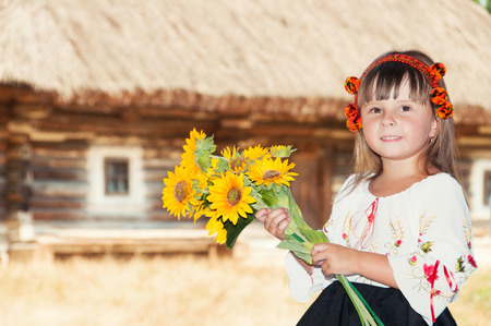 Girl with sunflowers and Hutsul wreath in the village with old wooden houseの写真素材