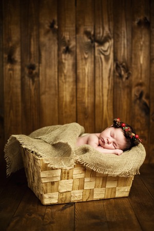 beautiful newborn sleeping baby girl in a wicker basket on a wooden backgroundの写真素材