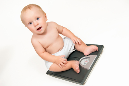 Baby boy check own weight on scales. White backgroundの写真素材