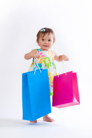 Little girl standing with colorful paper bags isolated on white background.の写真素材