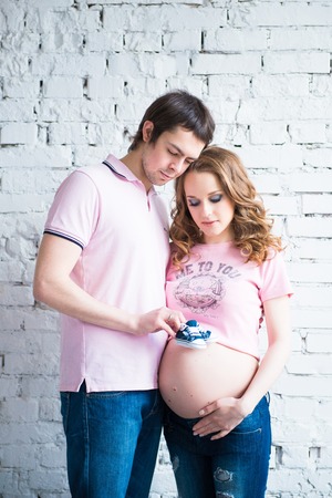 Childrens shoes in the hands of a young dad on the background of the belly of a pregnant womanの写真素材