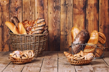 Different bread with ears in basket on wooden background