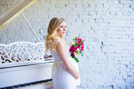 Beautiful pregnant woman with a bouquet of flowers in the interior waiting for the baby. Pregnancy.の写真素材