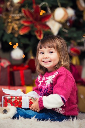 Happy girl with a gift in hands on a background of a New Year tree.の写真素材