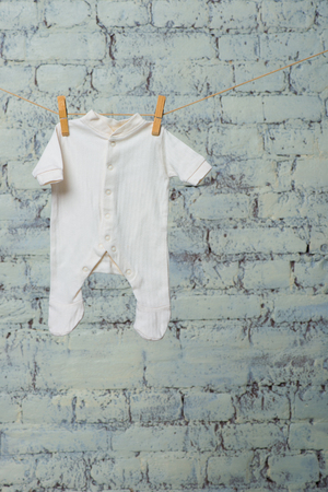 The childs white bodik dries on a rope against a white brick wall.の写真素材