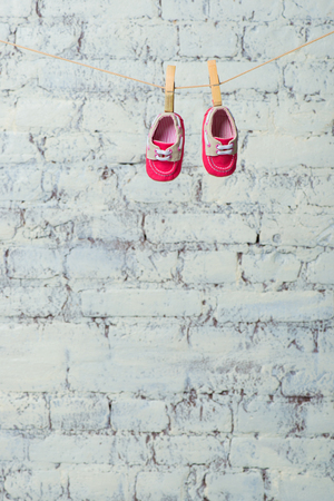 Baby red shoes on a rope against a white brick wall.の写真素材