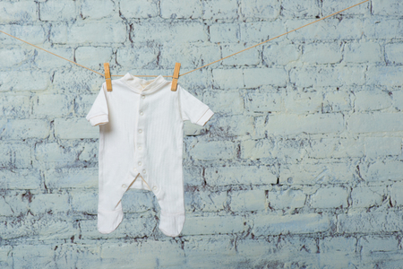 The childs white bodik dries on a rope against a white brick wall.の写真素材