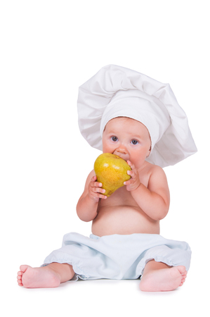 Cheerful little child with a pear in his hands in a chef suit on a white background.の写真素材
