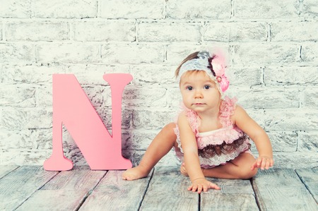 Beautiful and cute girl in pink dress with the letter N. Emotional girlの写真素材
