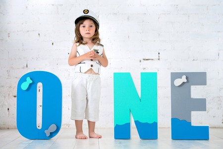 Happy child in a captains suit with the letters One on a white background of a brick wallの写真素材