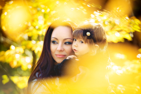 Little girl and her mother playing in the autumn parkの写真素材