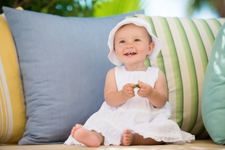 Cute little girl in a dress sits in pillows, smiling happilyの写真素材