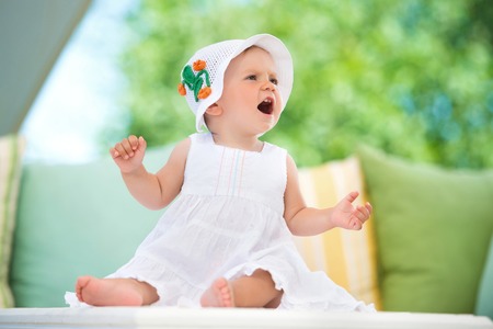 Cute little girl in a dress sits in pillows, smiling happilyの写真素材
