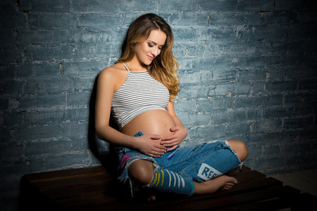 Young woman sitting in top and jeans. Pregnant blonde pending parenthood conceptの写真素材
