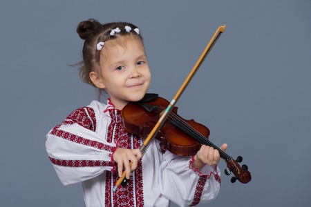 Girl playing the violin on plain gray background in studio. Girl dressed in Ukrainian embroideryの写真素材
