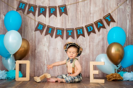 Happy birthday, little gentleman. The boy is dressed in a retro costume with suspenders, a cap and a bow tie and sits among the balloons. Child 1 year.の写真素材
