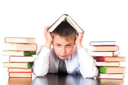 A tired, lagging schoolboy boy sits in a library with books and learns lessons. Unwillingness to learn.の写真素材