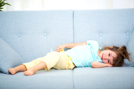 Cute little girl in home clothes lies in the room on the couch.の写真素材